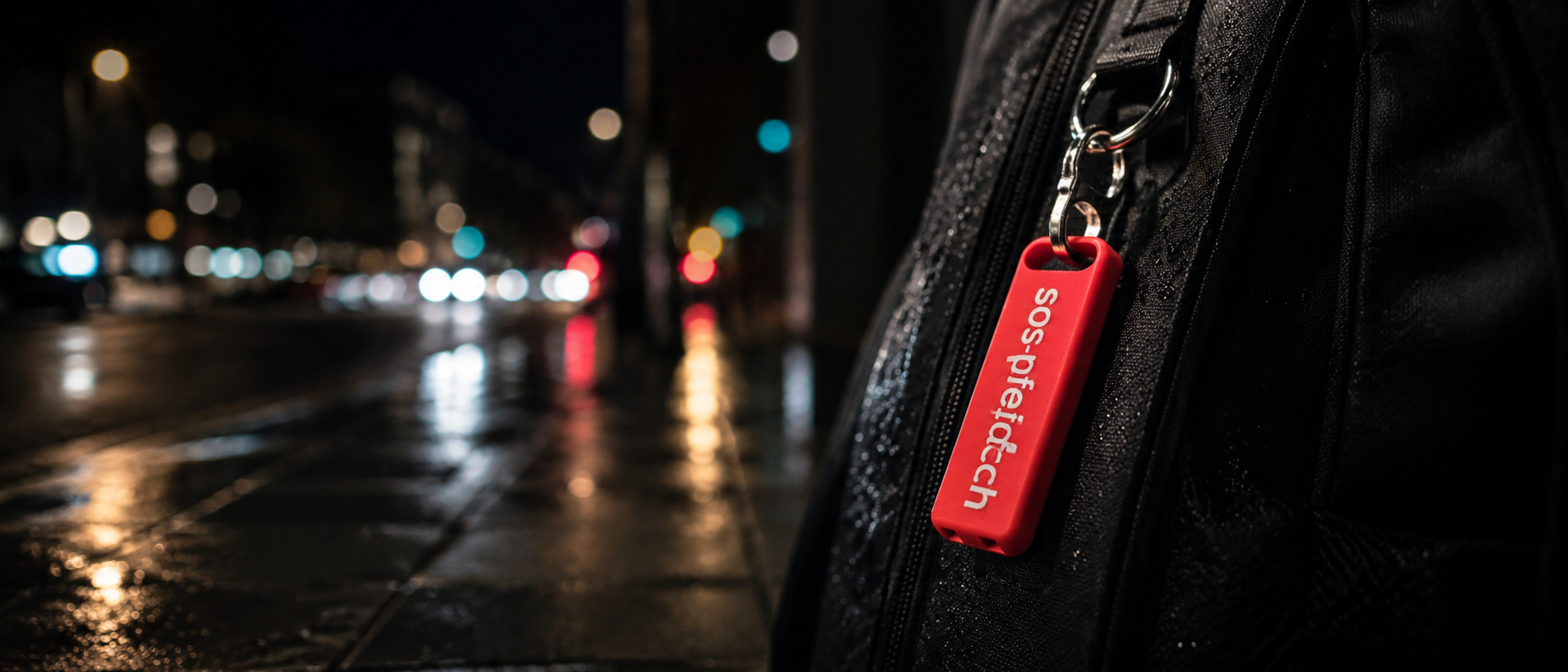 Rote SOS-Pfeife am Rucksack in einer nassen Stadtnacht